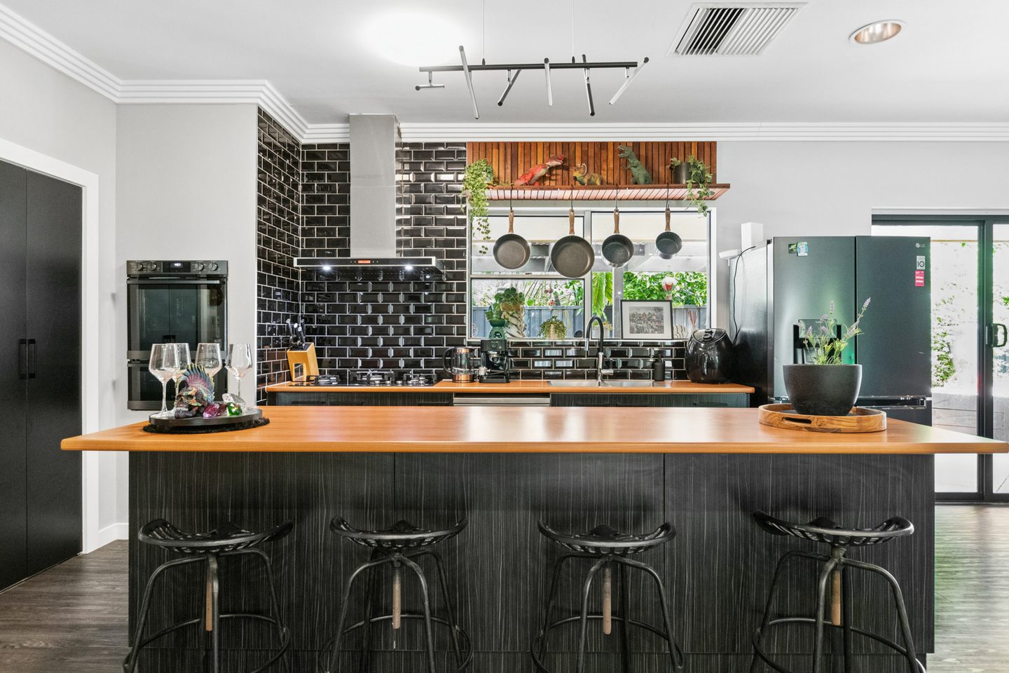 Black kitchen cabinetry and glossy tiles with a warm-toned island benchtop