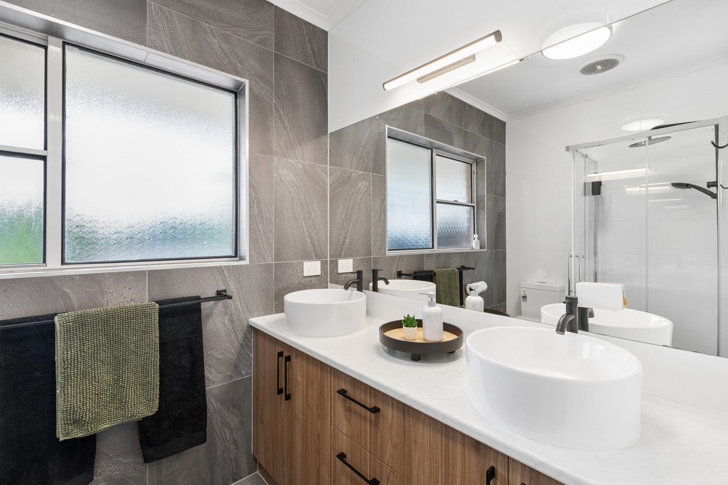 Bathroom with a wide vanity, countertop basins and grey tiles
