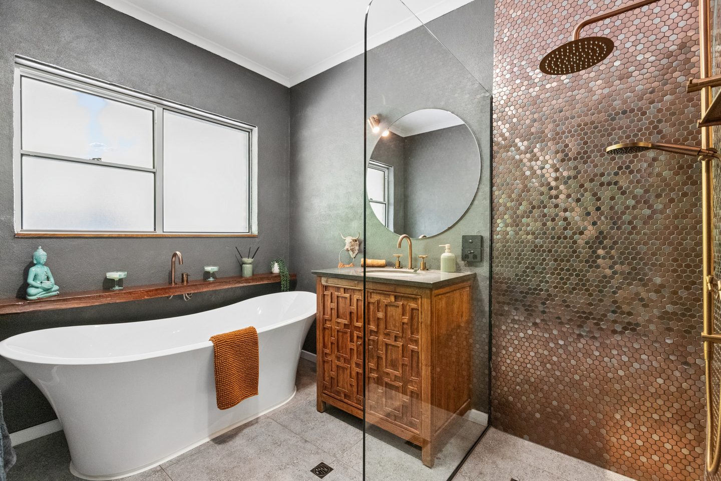 Bathroom with freestanding bath, patterned vanity and copper-toned shower tiles