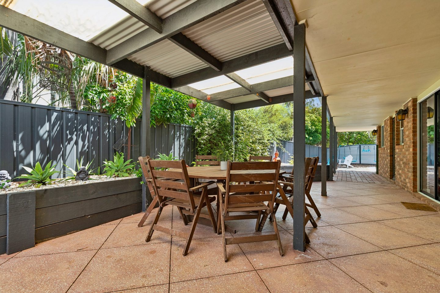 Covered paved entertaining area beside raised garden beds and the brick house
