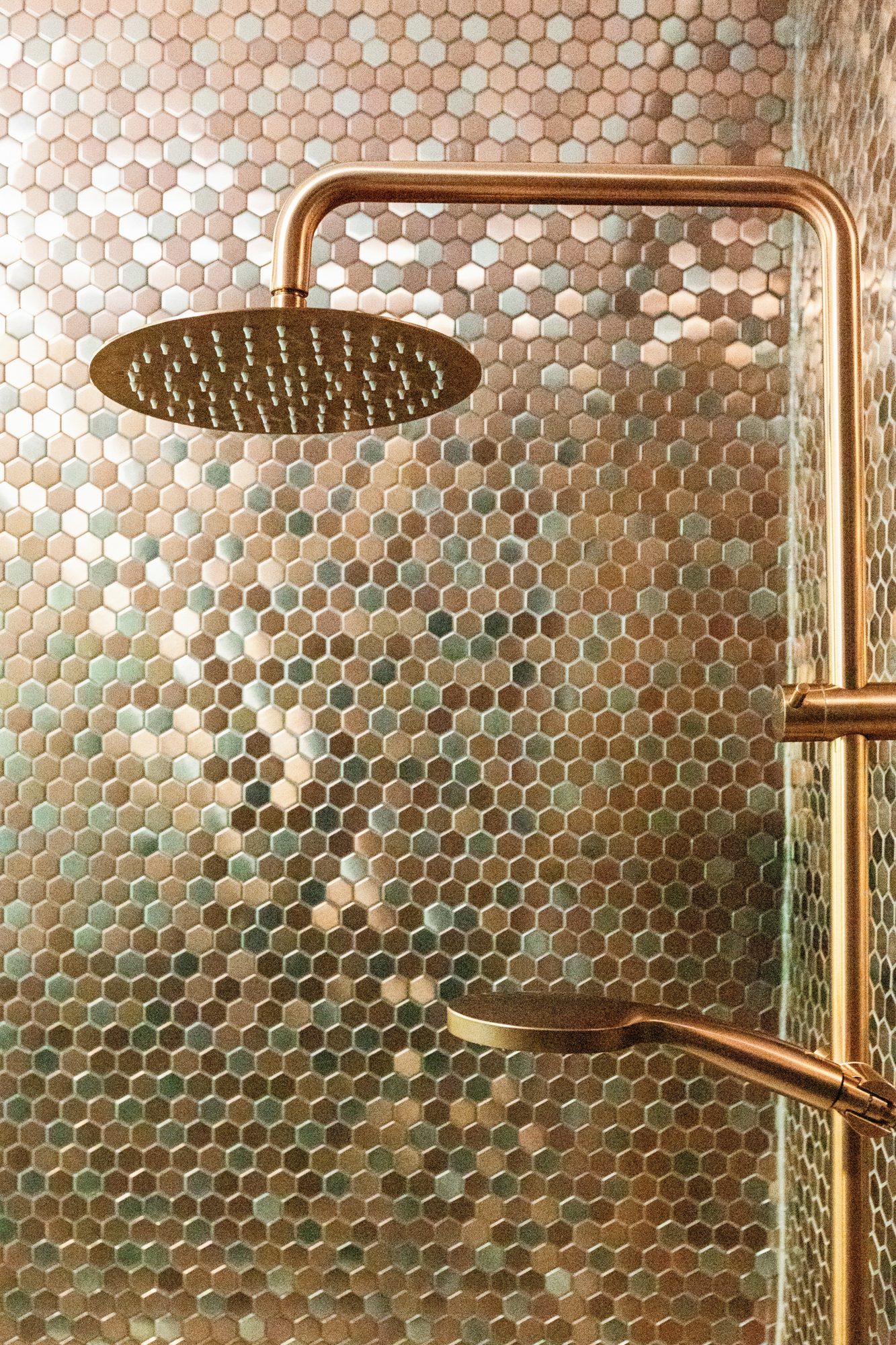 Hexagonal copper-toned shower tiles and warm-toned shower fittings
